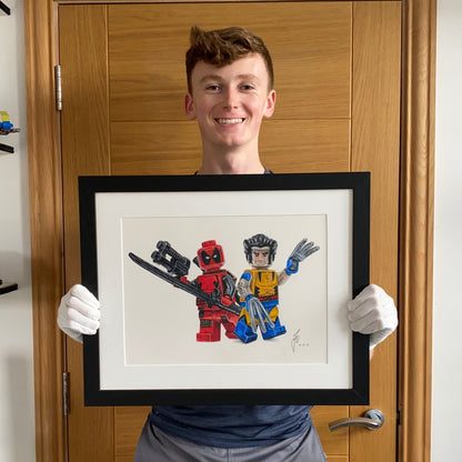 Tom Mothersole holding realistic coloured pencil drawing of th LEGo Deadpool and wolverine minifigures