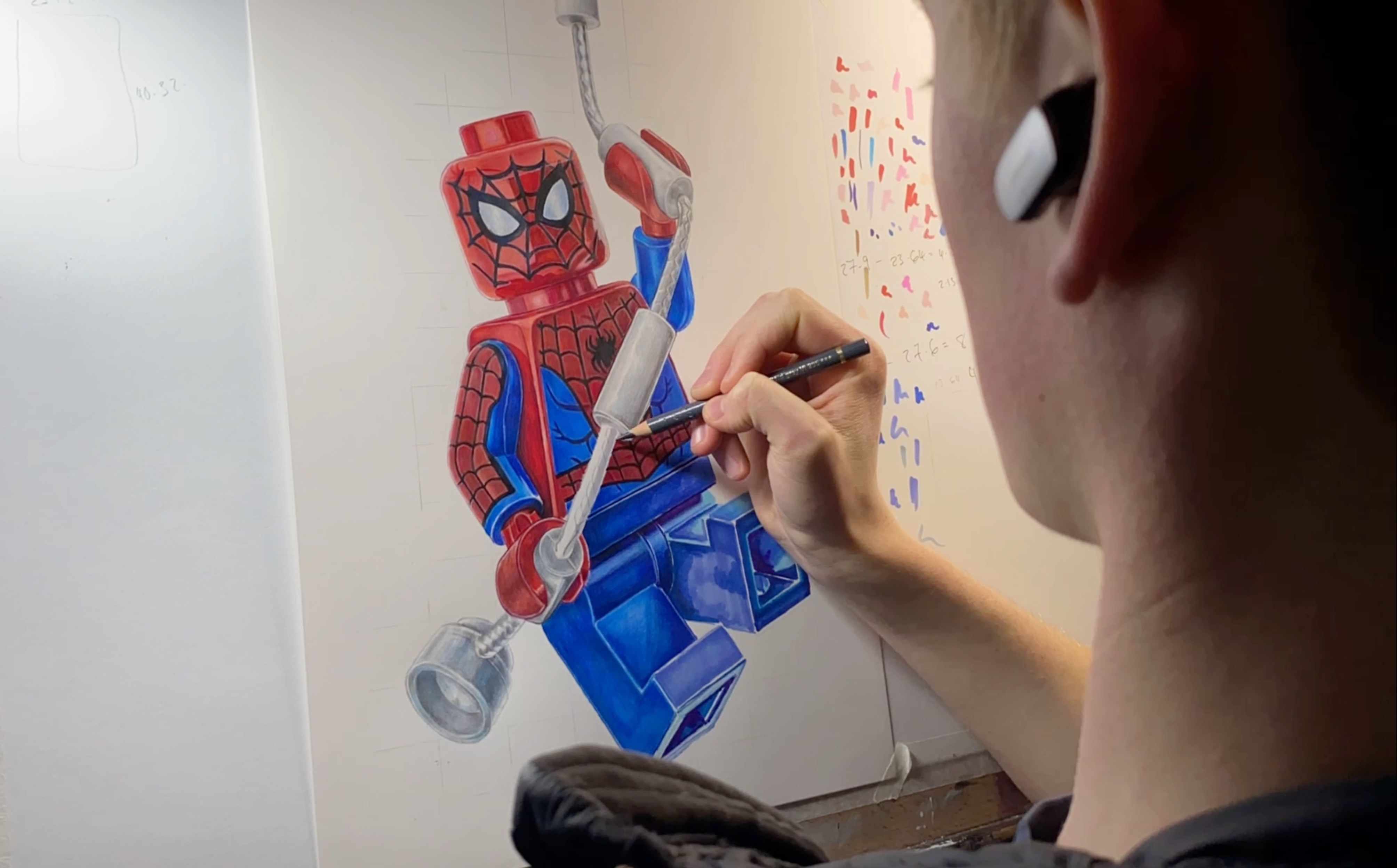 tom mothersole drawing a LEGO Spider-Man figure on paper with a pencil.