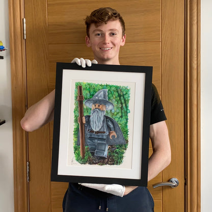 tom mothersole holding realistic coloured pencil drawing of the LEGo Gandalf minifigure from lord of the rings
